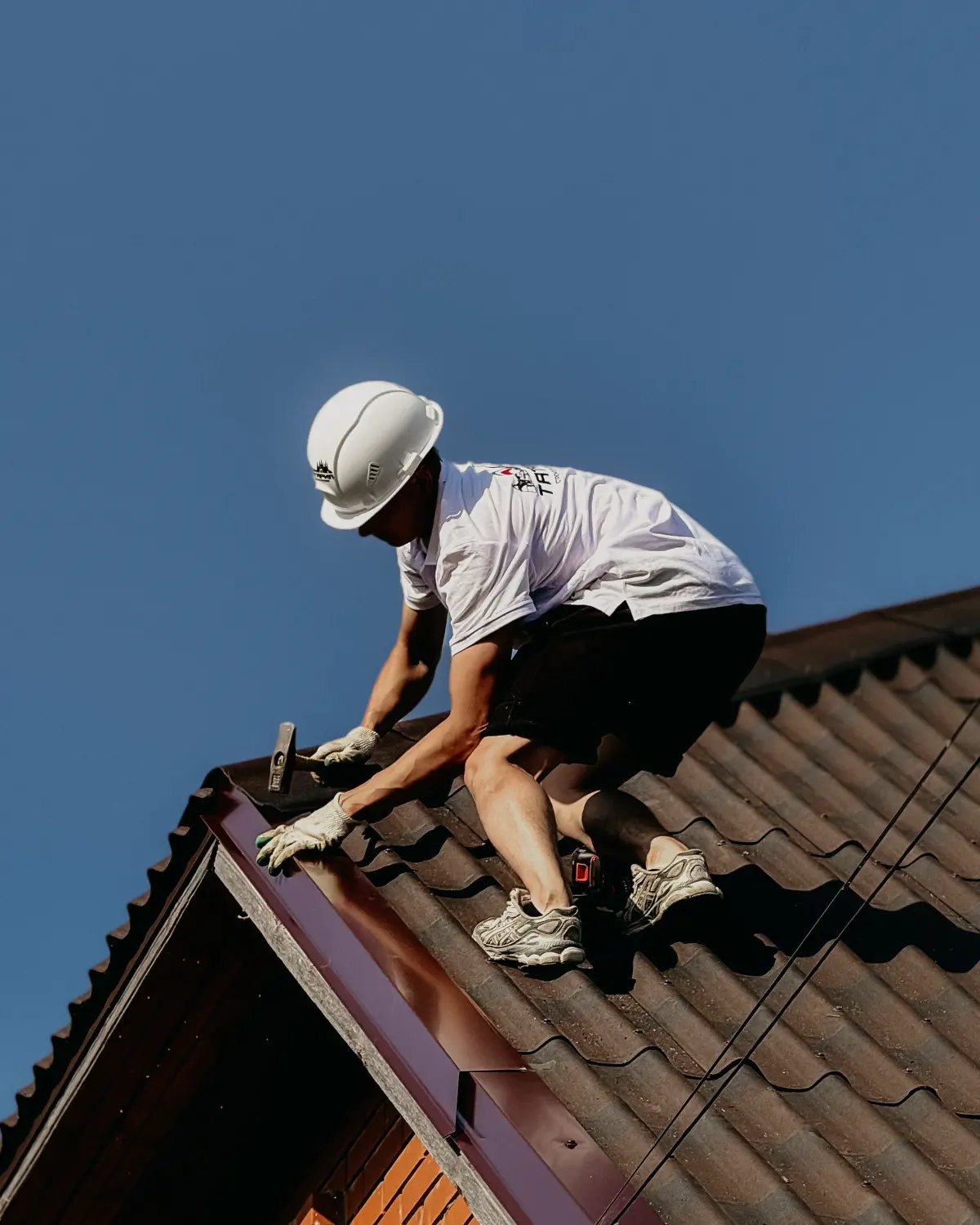 Un couvreur casqué pose des tuiles sur une toiture