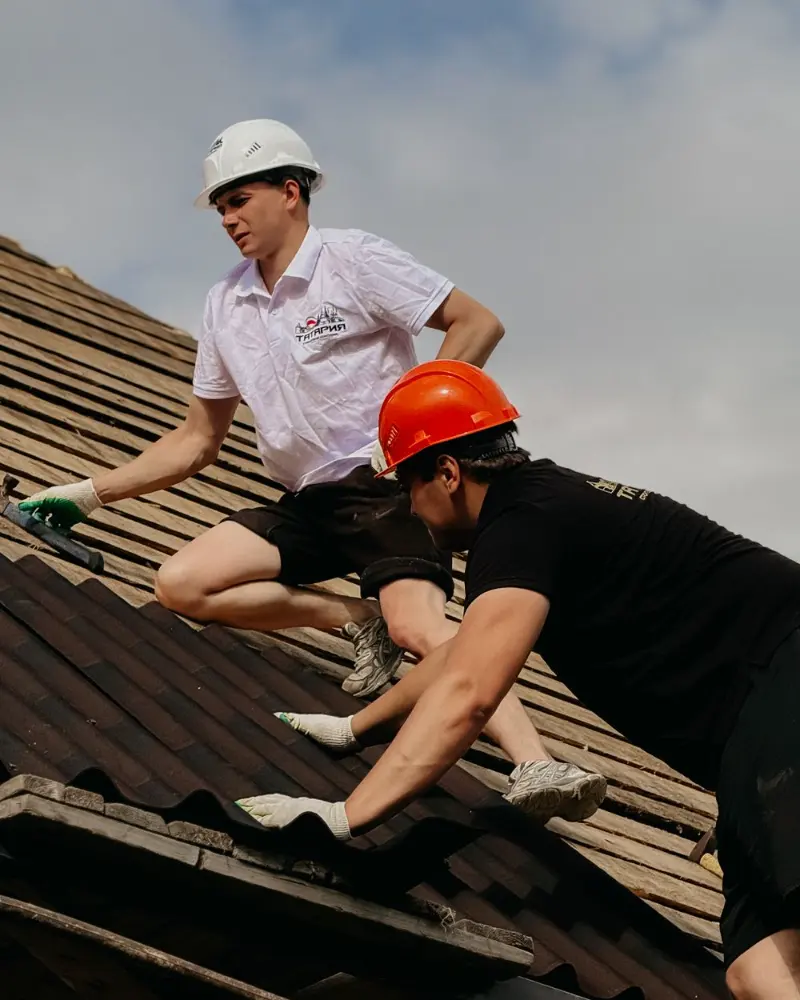 Deux couvreurs réparent une toiture en tuiles